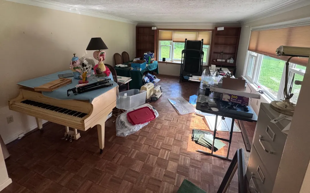 Before: a living room crowded with a piano, a desk, boxes and a filing cabinet.