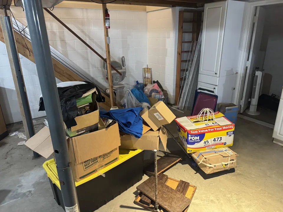 Before: boxes, a storage tote, bags and an old cart piled near basement stairs.